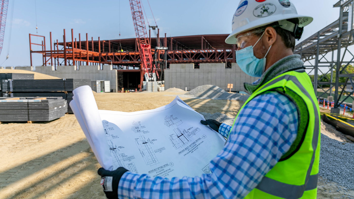 a project manager reviews a building design plan on-site during the COVID-19 pandemic