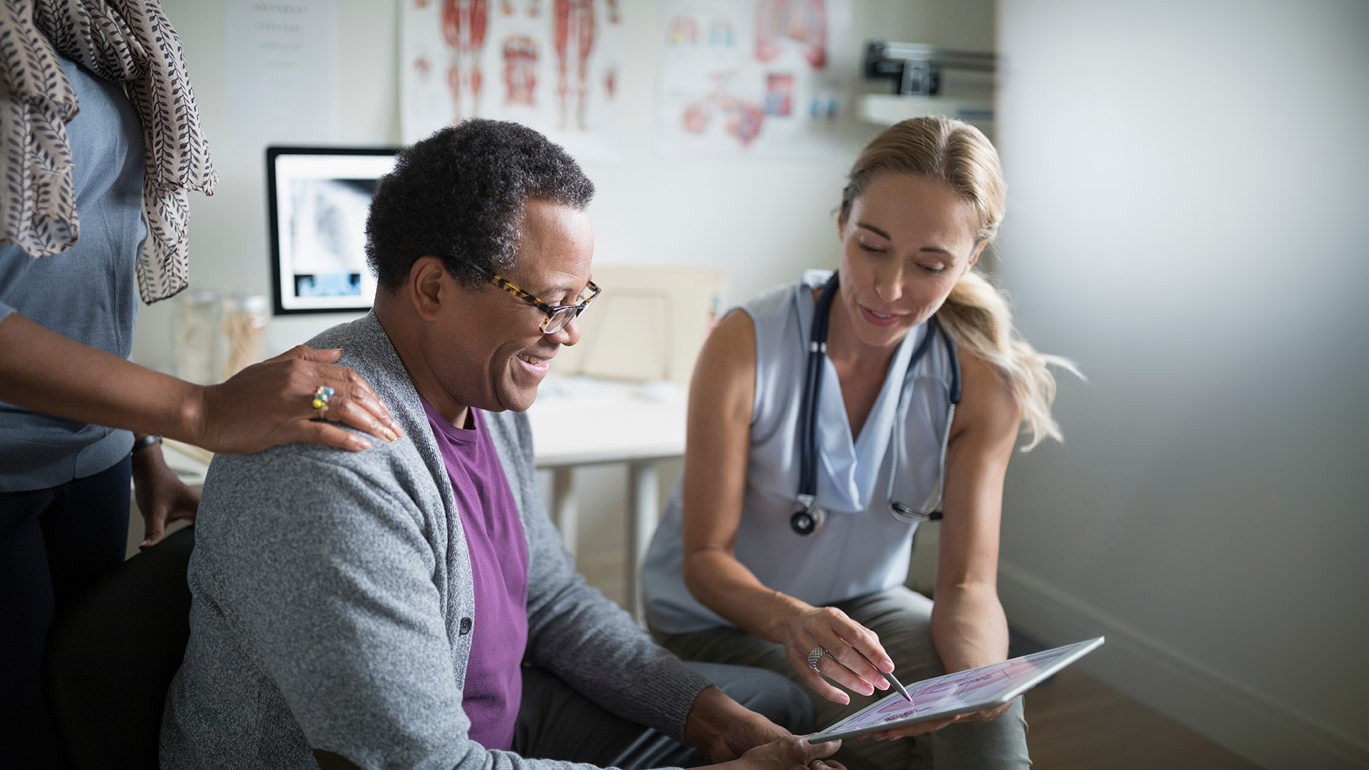 Female doctor showing digital tablet to senior male patient in examination room