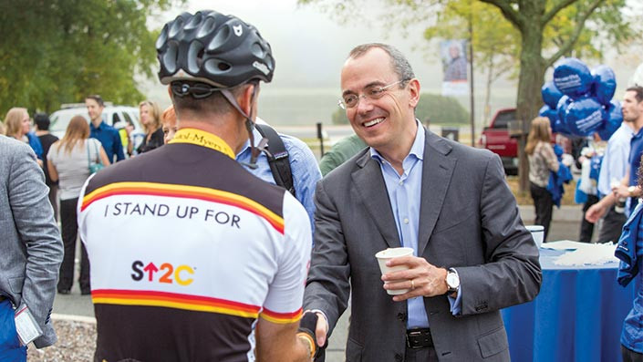 Giovanni Caforio shaking hands with a cyclist
